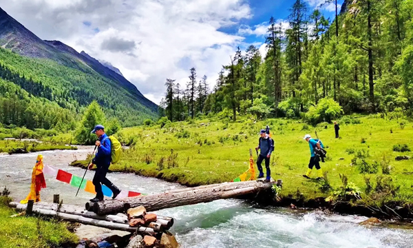 Trekkers carrying backpacks and hiking poles while crossing a stream in Mount Siguniang