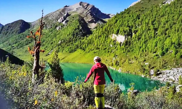 hiker beside a clear alpine lake in Qizanggou Valley